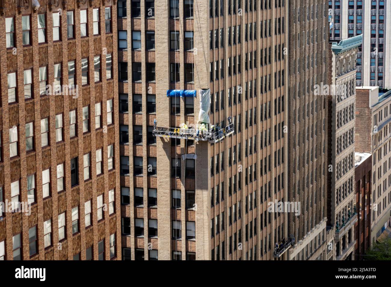 Team Of Workers replacing Bricks on an office Building Facade While working in a hanging rig 15 Stories Up , NYC, USA, 2022 Stock Photo