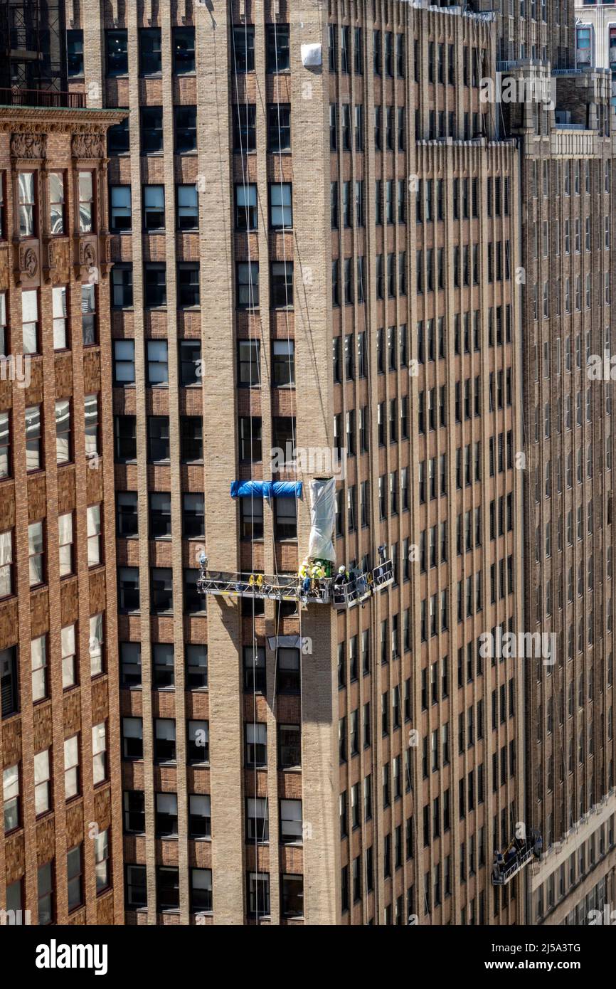 Team Of Workers replacing Bricks on an office Building Facade While working in a hanging rig 15 Stories Up , NYC, USA, 2022 Stock Photo