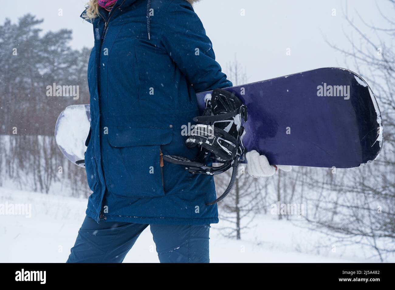 The girl holds a snowboard in her hands, she is dressed in a mountain jacket and a helmet Stock Photo