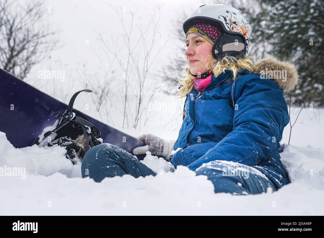 Portrait of a girl snowboarder in the snow. A girl in a ski helmet and a jacket lies on the snow. Stock Photo