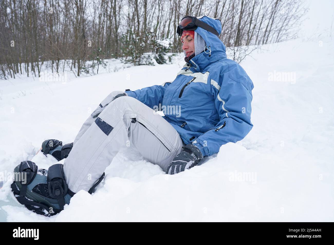 A guy with a snowboard is resting sitting on the snow Stock Photo