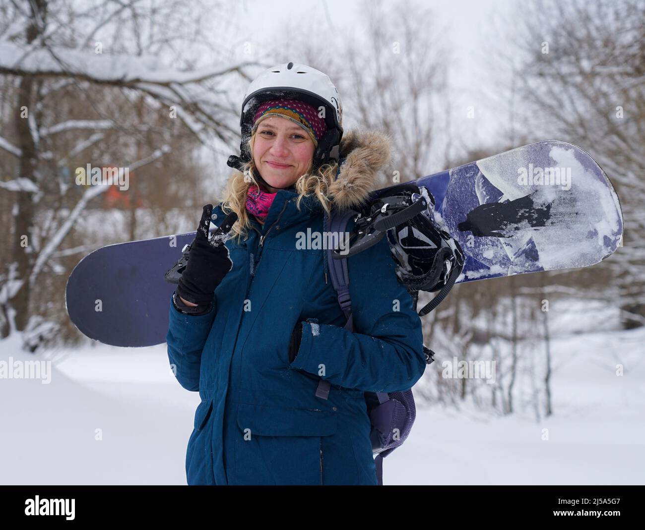The girl holds a snowboard in her hands, she is dressed in a mountain jacket and a helmet Stock Photo