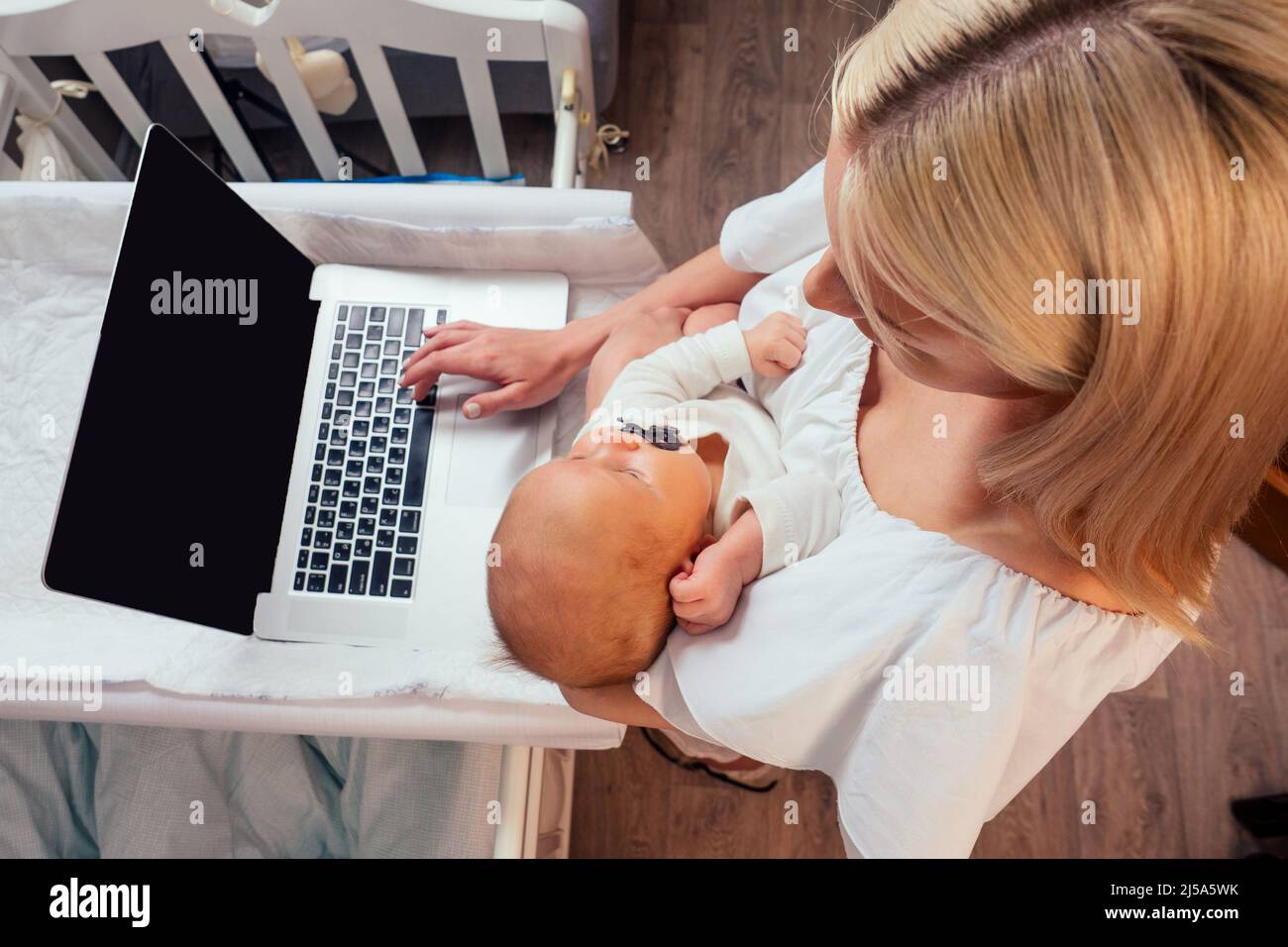 Happy single blonde mother working online and taking care of her baby surfing question on the internet Stock Photo