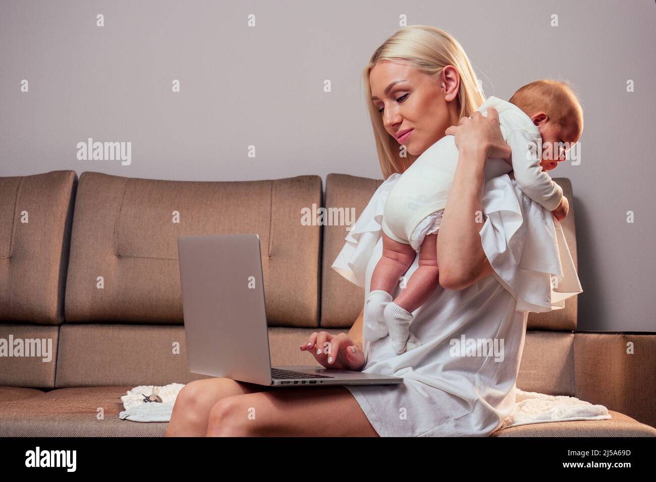 Happy single blonde mother working online and taking care of her baby surfing question on the internet Stock Photo