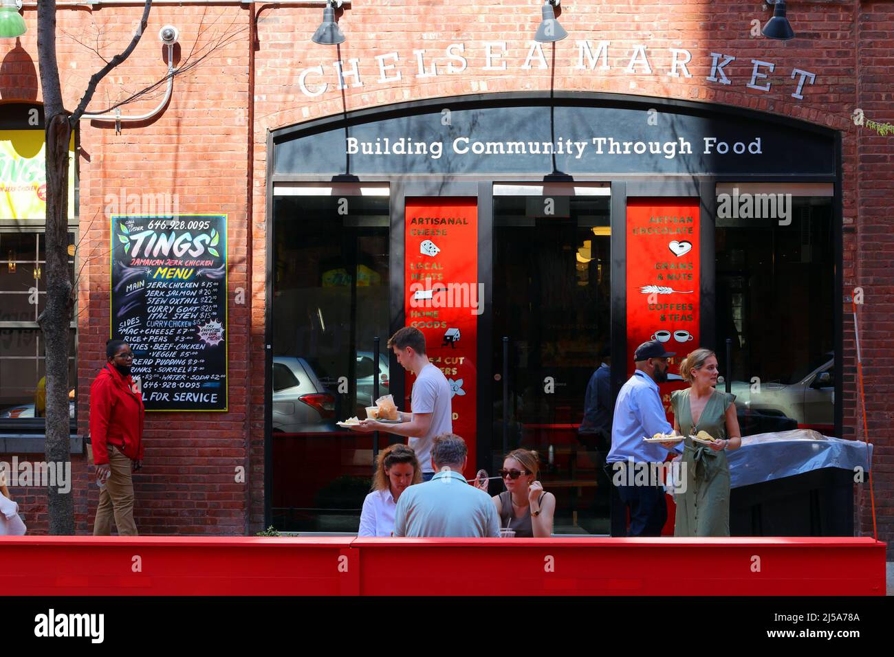 People carrying plates of food from Los Tacos No 1 food stall in the Chelsea Market look for seating outside at the W 15th St sidewalk dining area Stock Photo