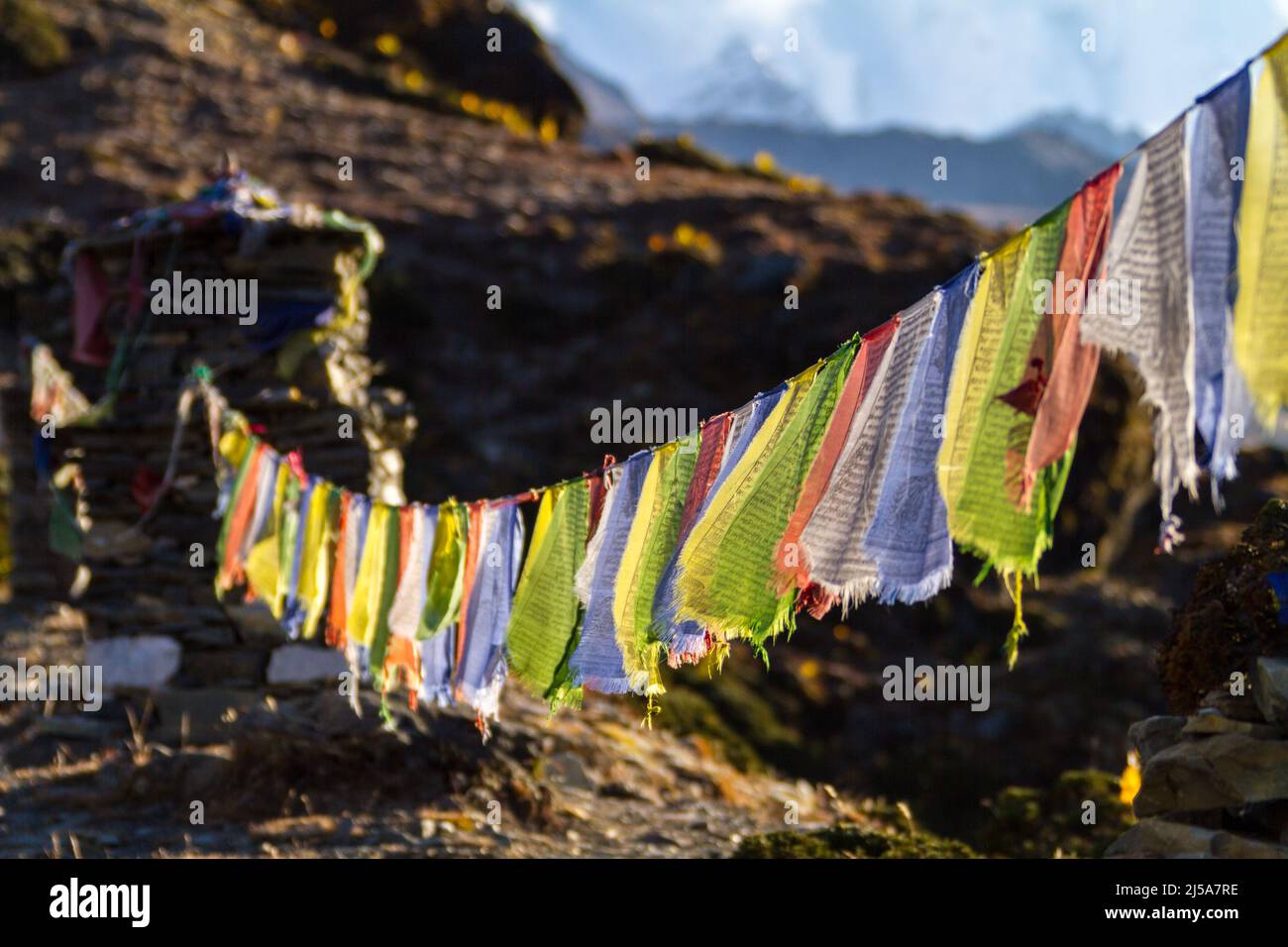 Buddhist prayer flags fly in front of distant snowcapped mountains in the Solukhumbu Region of the Nepali Himalayas - Dingboche - Nepal Stock Photo