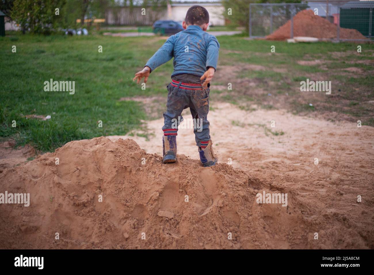 A child plays with the sand. The boy in the sandbox. Naughty boy stained clothes on the playground. A child jumps in the sand. A hyperactive child doe Stock Photo