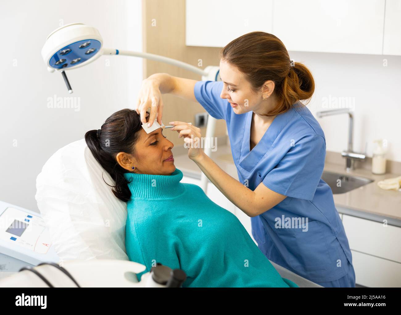 Beautician using white pencil and ruler for marking skin of latin woman ...