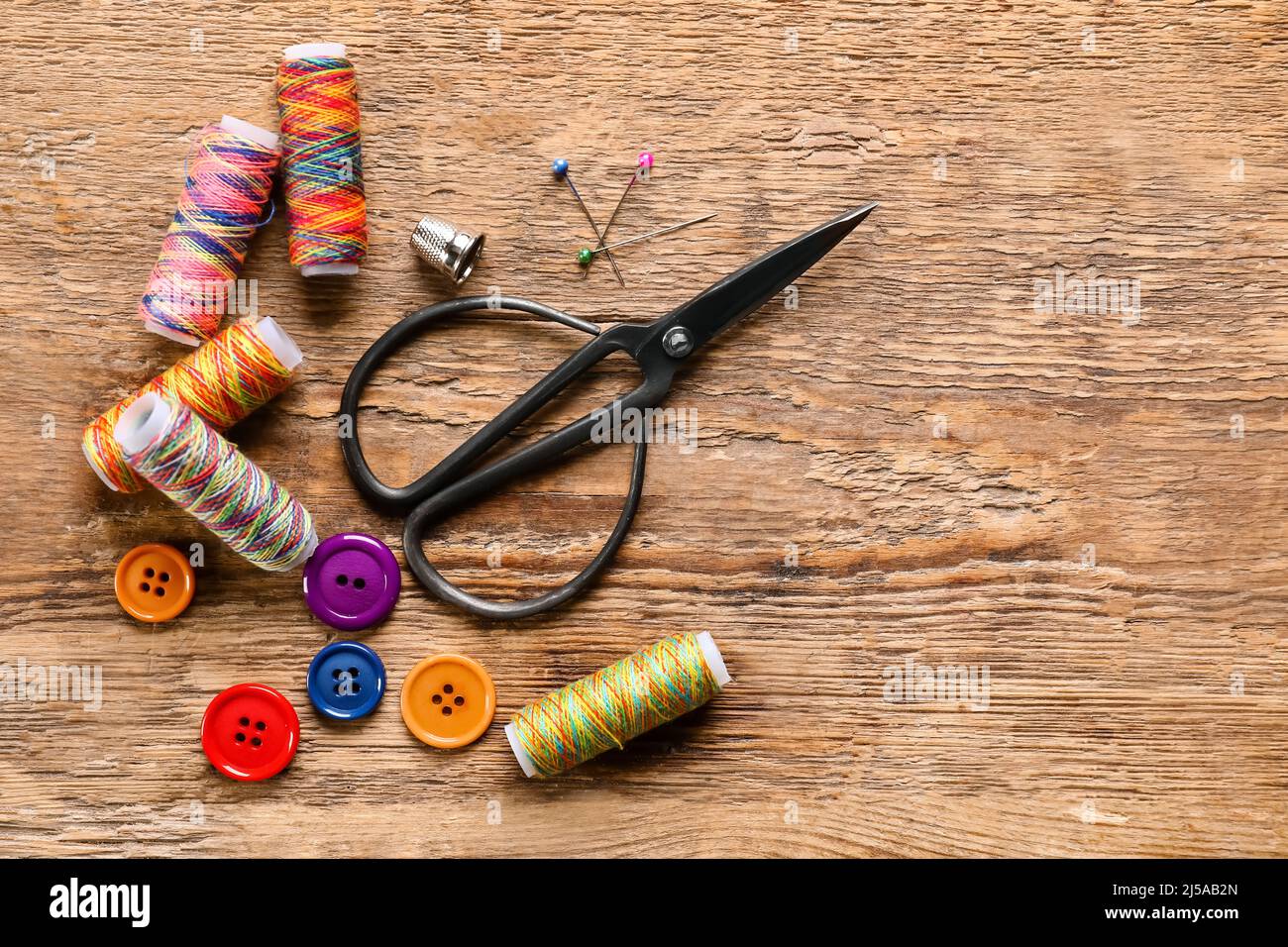 Sewing threads with buttons and scissors on wooden background Stock Photo