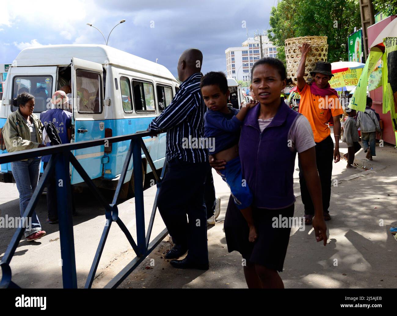 A Malagasy woman carrying her child next to a public bus in Antananarivo, Madagascar. Stock Photo