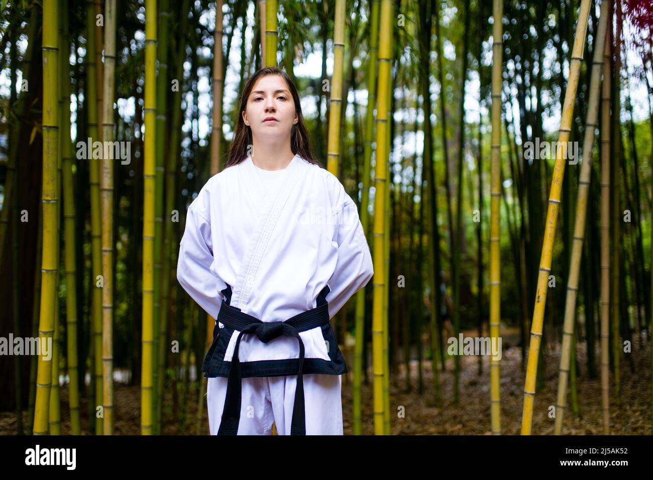 A young woman with a black belt coaches in martial art outdoor bamboo background Stock Photo