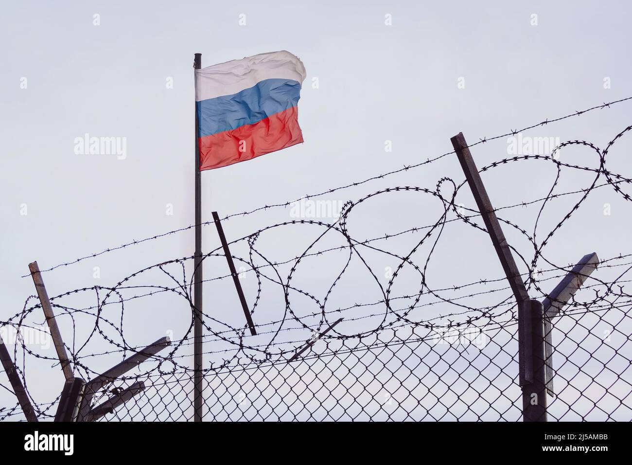 View of russian flag behind barbed wire against cloudy sky. Concept anti-Russian sanctions. A border post on the border of Russia. cancel culture Russ Stock Photo