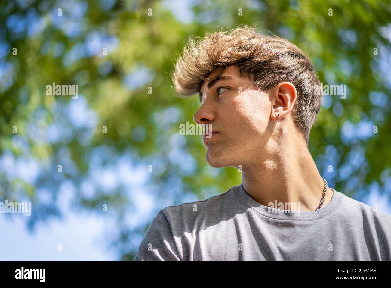 Confident young blonde man portrait, summer trees background. Copy space Stock Photo