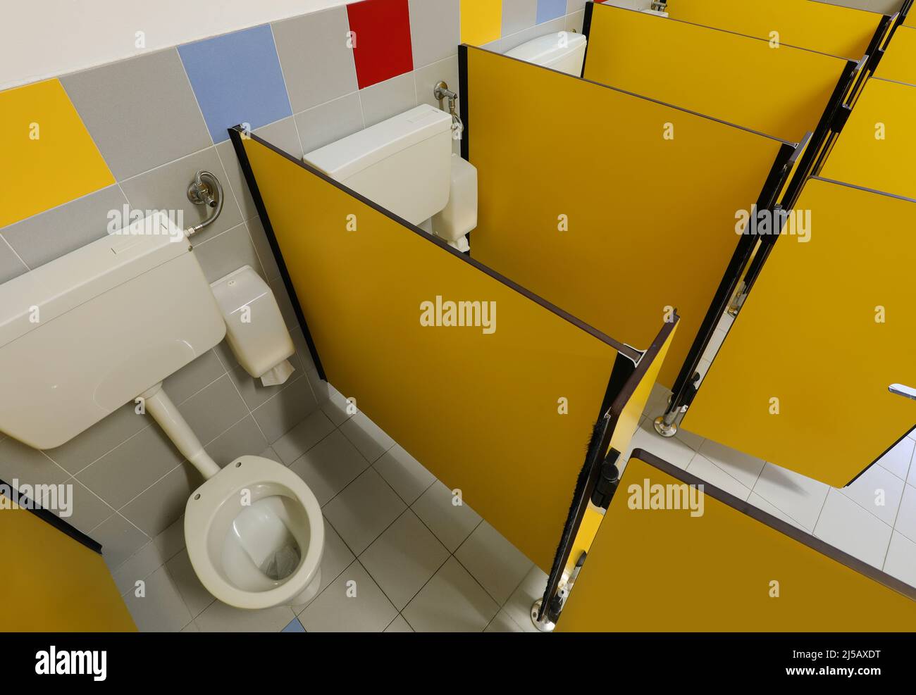interior of the nursery school bathrooms with low ceramic toilets and yellow toilet cubicles without children Stock Photo