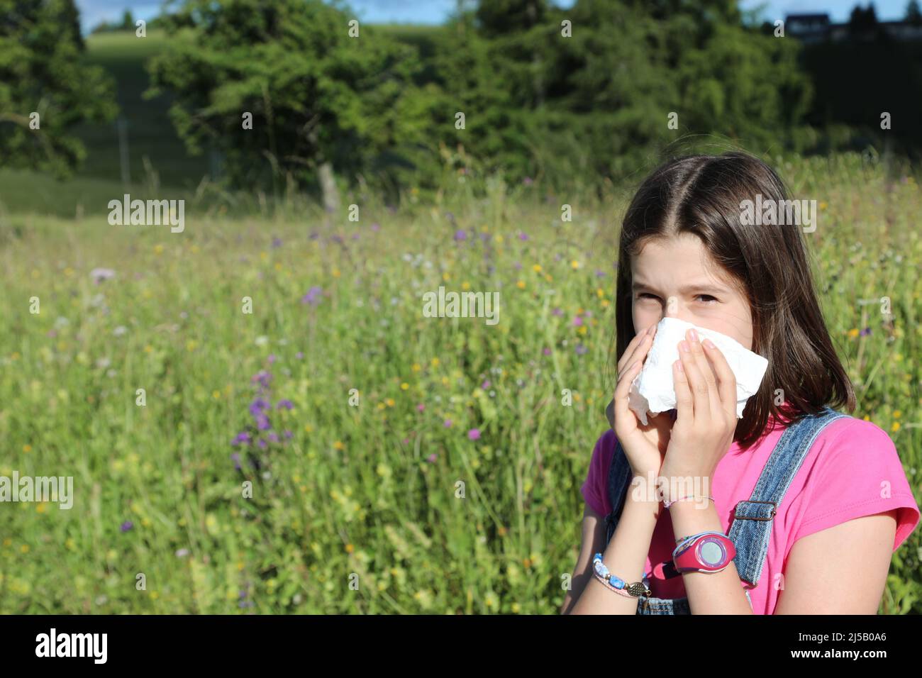 young girl blows her nose with handkerchief in spring due to grass allergy Stock Photo