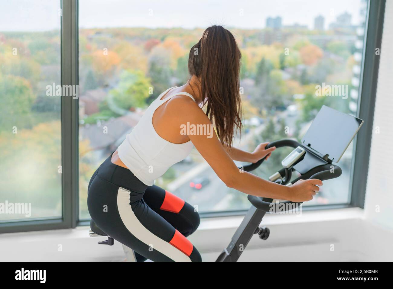Exercise at home indoor cycling with online class on screen. Woman training cardio biking on workout spin bike active fitness lifestyle Stock Photo