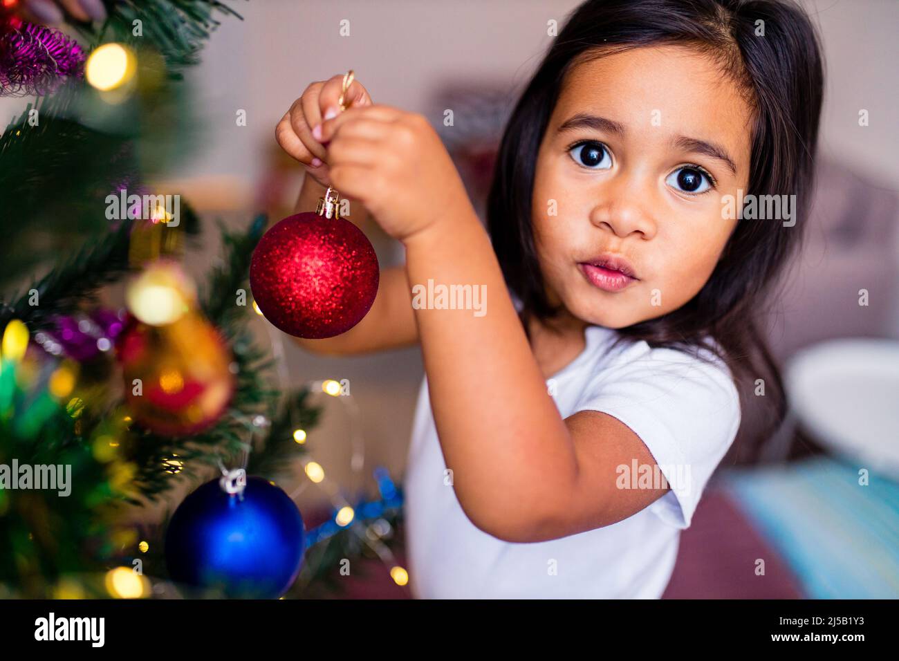 mixed race little cute girl decorating a christmas tree in the xmas morning in bedroom and wishing a wish Stock Photo