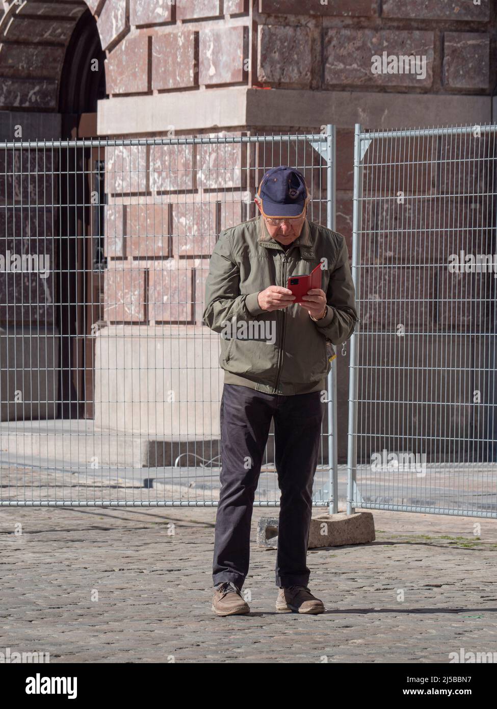 Antwerp, Belgium, April 17, 2022, Elderly man with a cap on his head searches for tourist information on his smartphone on the market square in Antwer Stock Photo