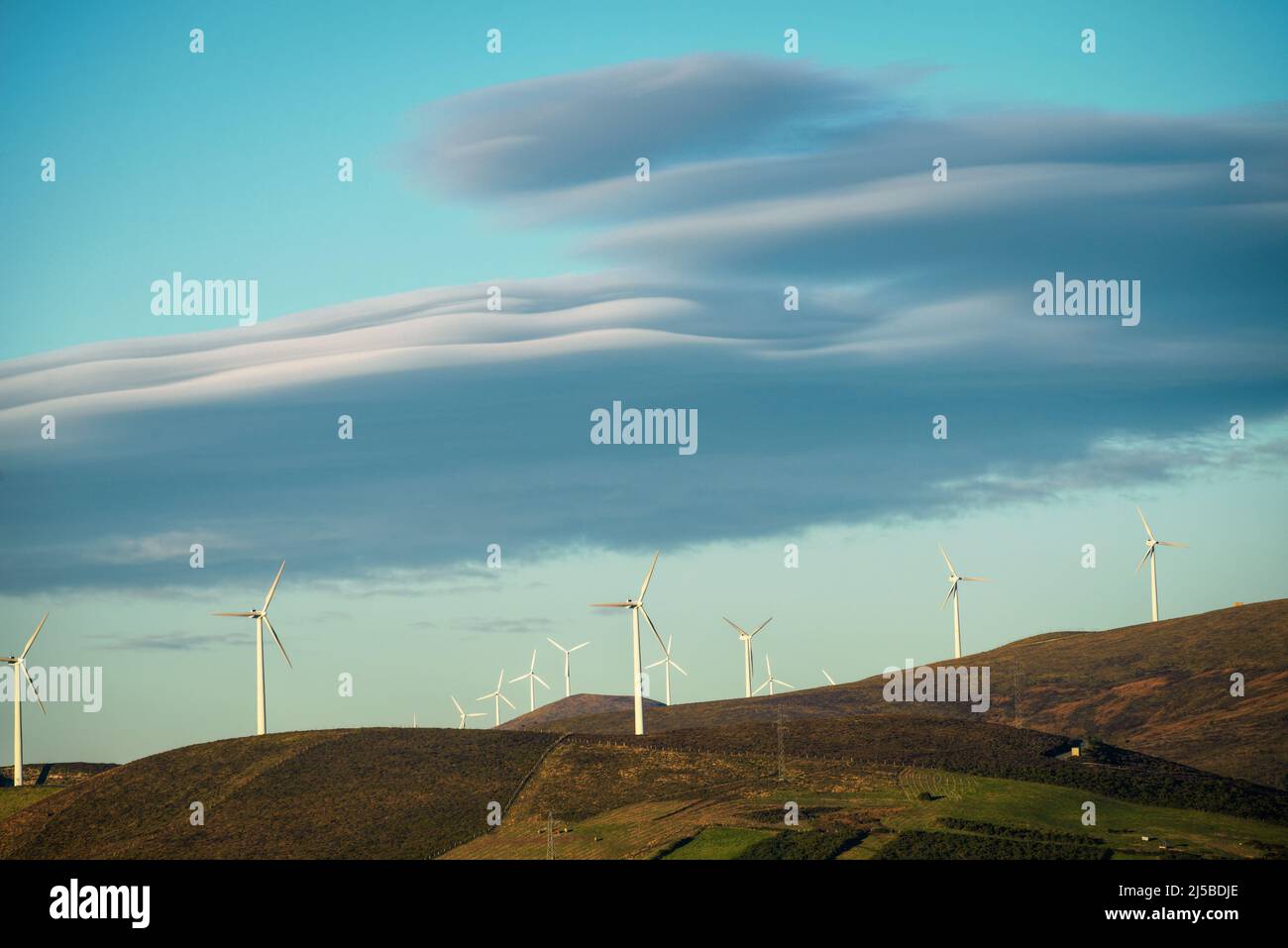 Lenticular clouds over wind farms and meadows with horses in Muras Xistral in Lugo Galicia Stock Photo