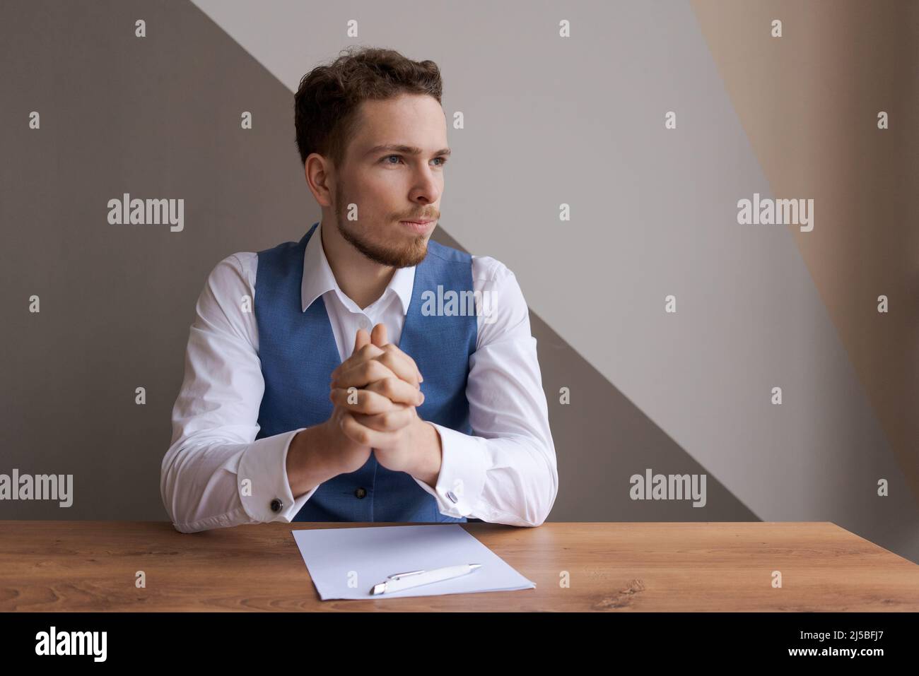 Young businessman with beard sits in office at table with documents and thinks about successful signing deal and the conclusion contract. Interview or discussion of plans for business development Stock Photo