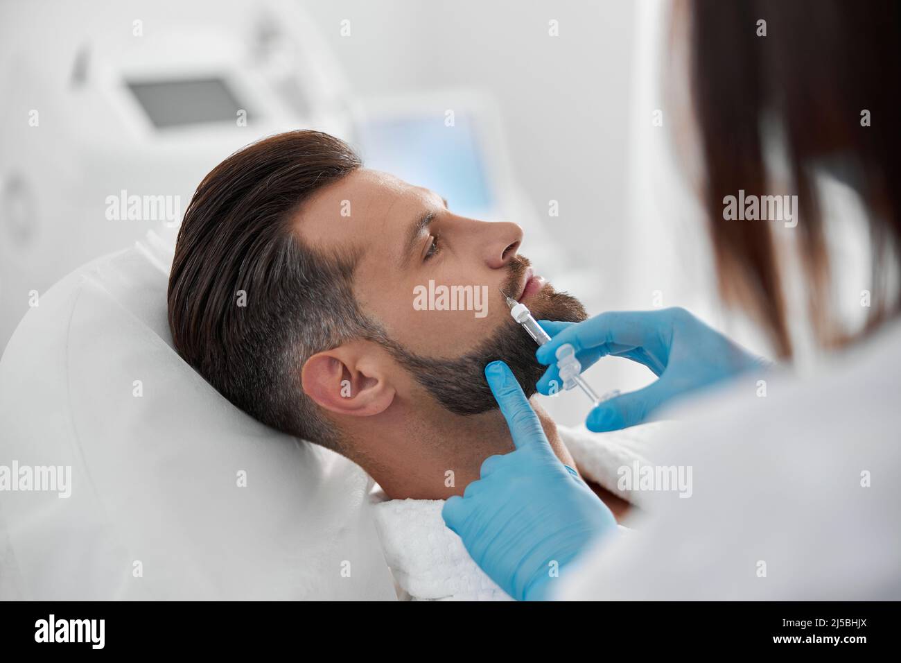 Middle aged man with beard undergoes nasolabial fold filler procedure with beautician in clinic Stock Photo