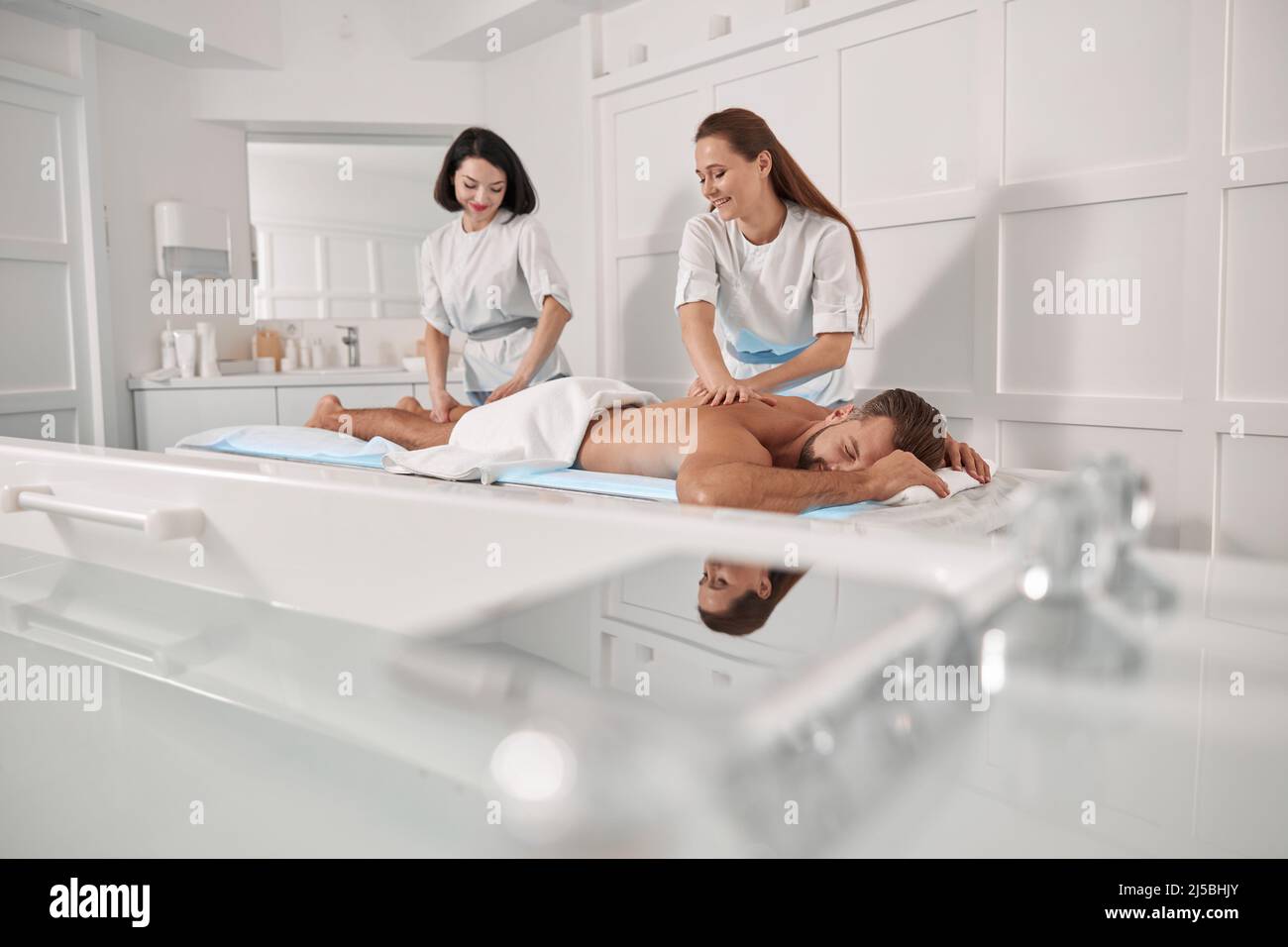 Smiling women in uniforms do massage to middle aged man patient in hospital Stock Photo