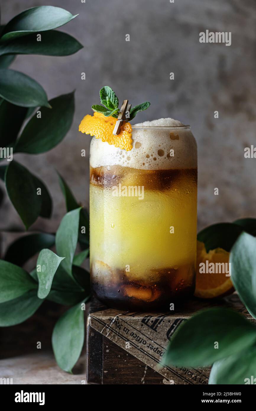 Trendy coffee shop seasonal drink: iced coffee with orange juice and caramel syrup. Bumble coffee in a glass with ice and mint on dark background. Men Stock Photo