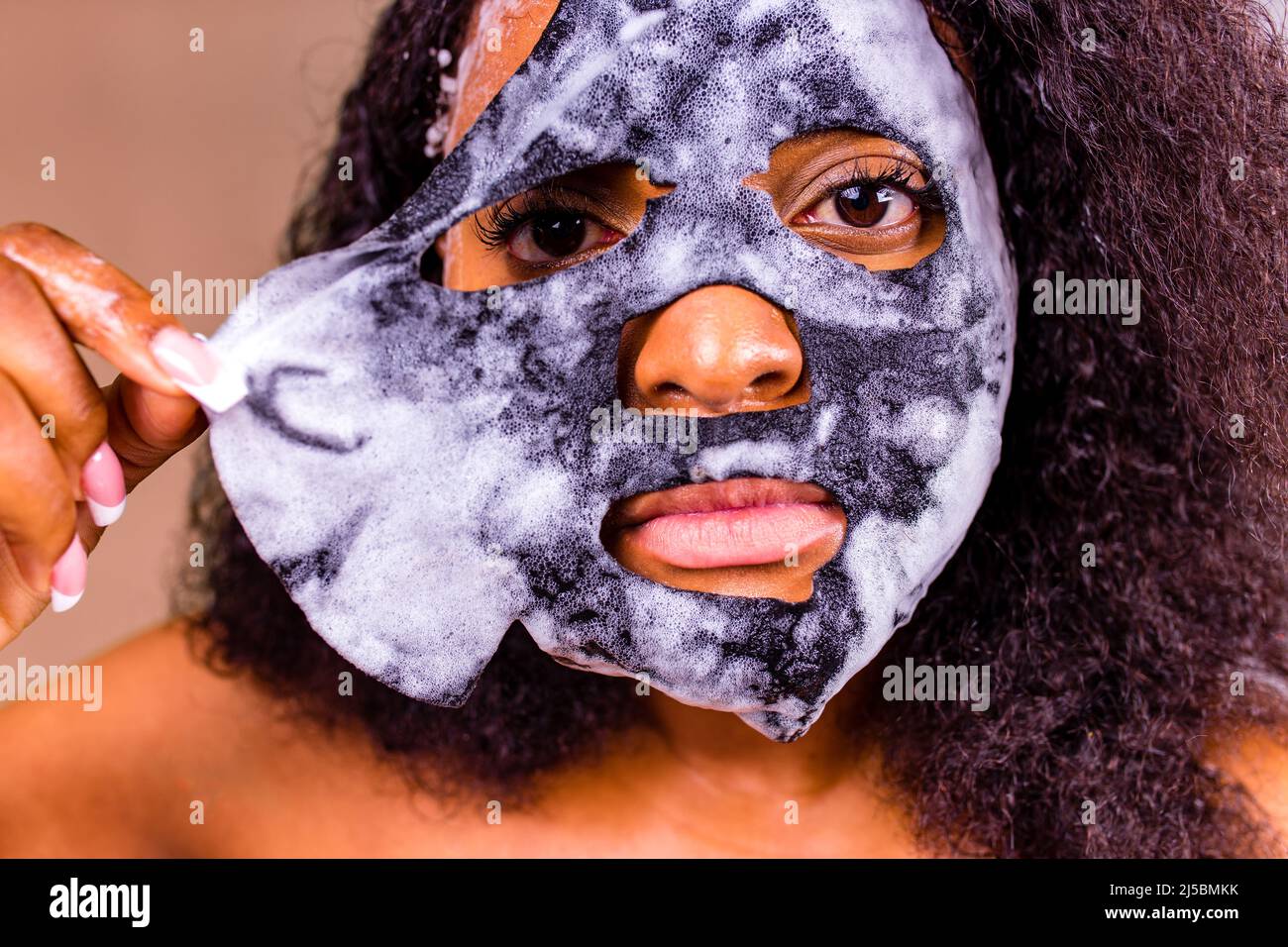 Young woman with bubble sheet mask on her face on brown background Stock Photo