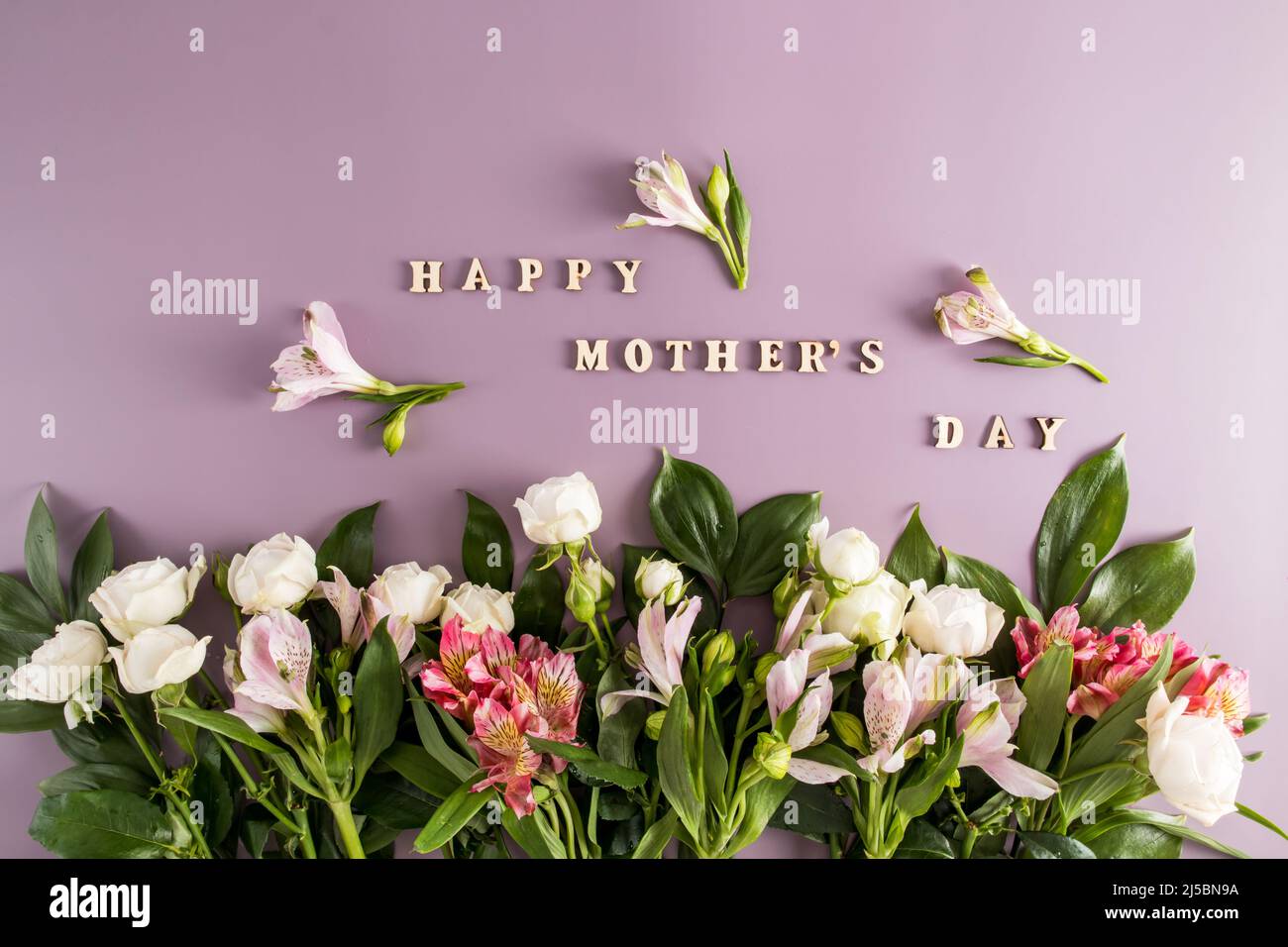 Holiday concept with bouquet of Alstroemeria flowers and roses on pastel pink background. Wooden text happy mothers day. Festive greeting card Stock Photo