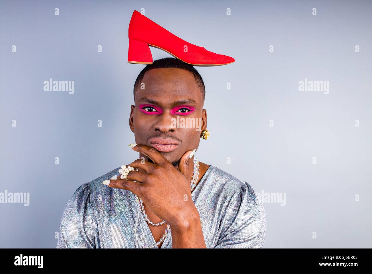 african american cross dressing trans drag queen holding a red shoe in studio white wall Stock Photo
