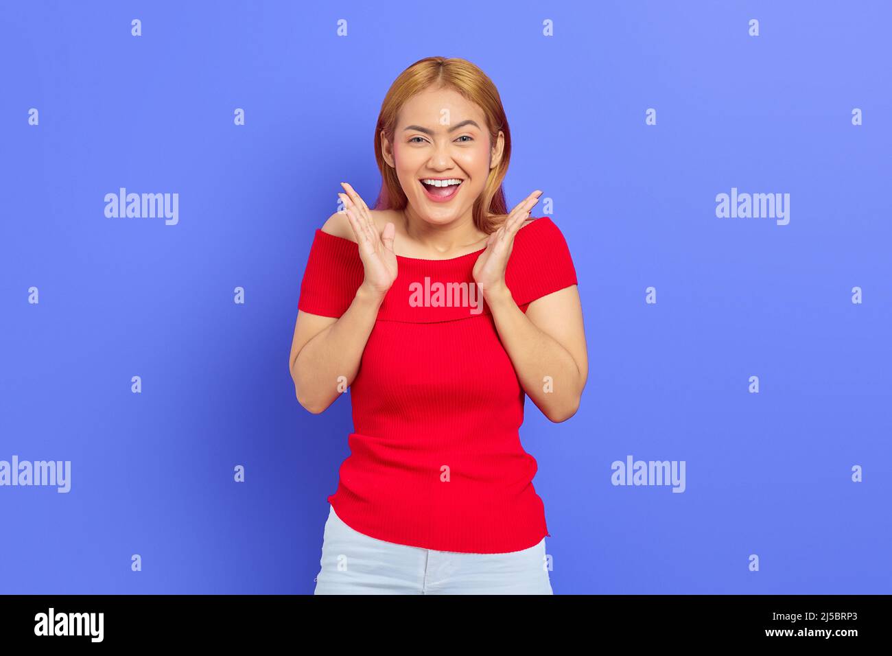 Portrait of cheerful young Asian woman in red dress raising hands over ...