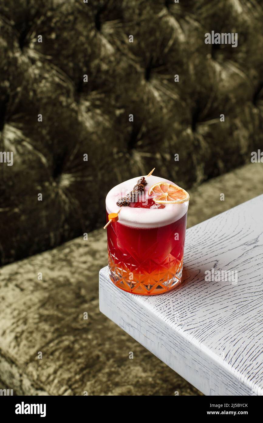 Glass of a New York sour cocktail decorating with small pine cone and orange zest standing on