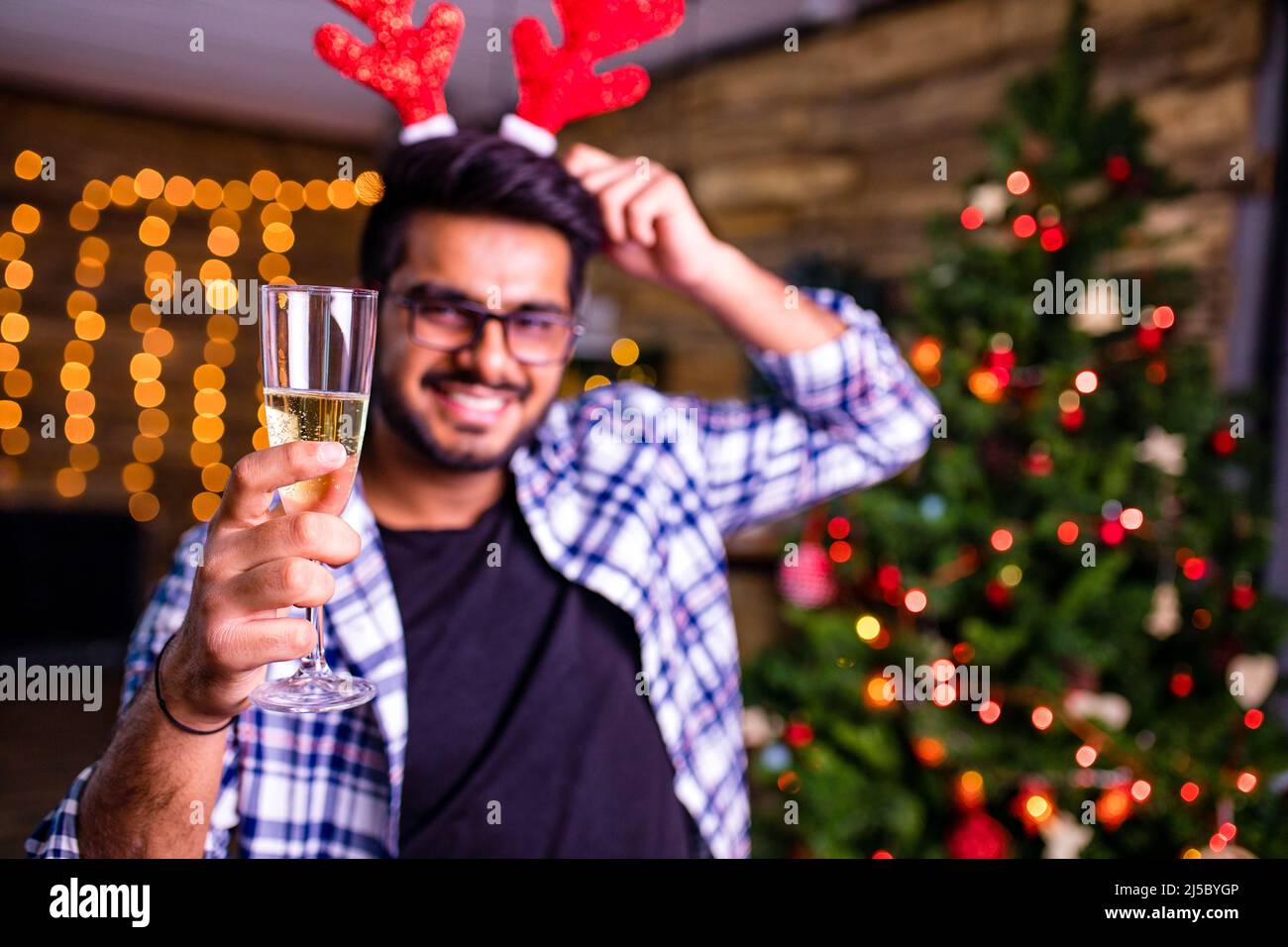 indian man with deer horn on head drinking alcohol at studio shot spruce Christmas tree lights garland background Stock Photo