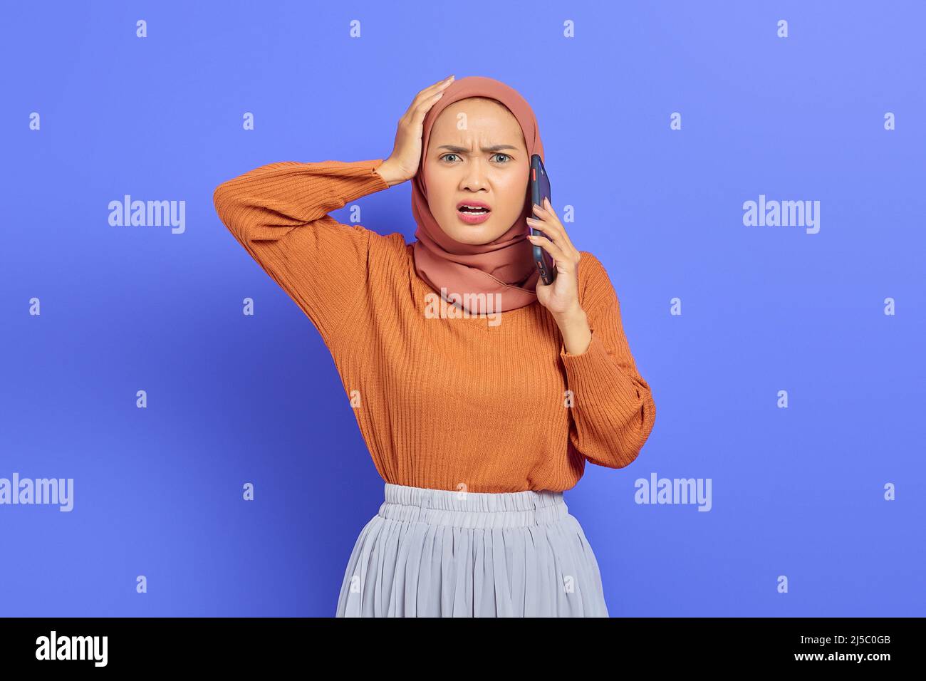 Shocked beautiful Asian woman in brown sweater talking on mobile phone