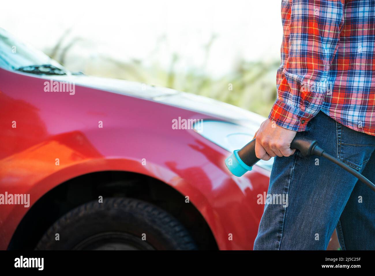 Male model stands by an electric car and holds a charging plug Stock Photo