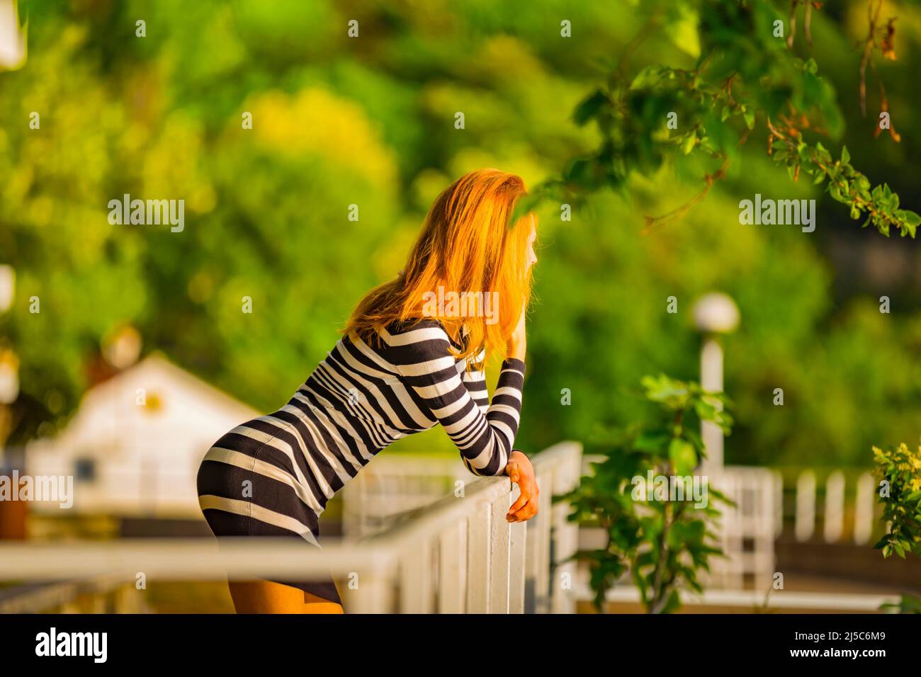 Adolescent teen girl bending bend over bendover inclined on fence in park golden hair blonde prone posture Stock Photo