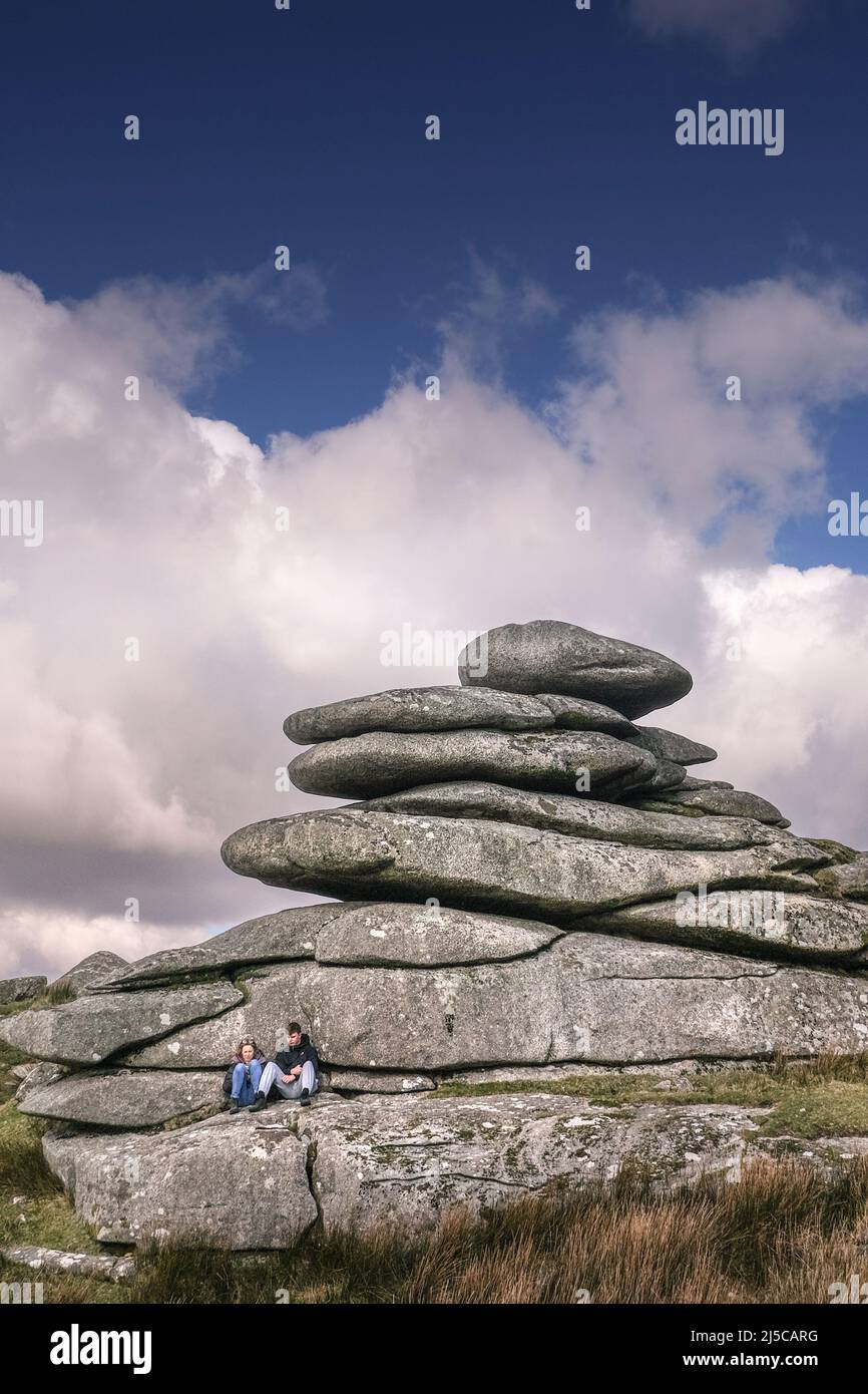 A young couple relaxing under a towering granite rock stack left by glacial action on Stowes Hill on Bodmin Moor in Cornwall. Stock Photo