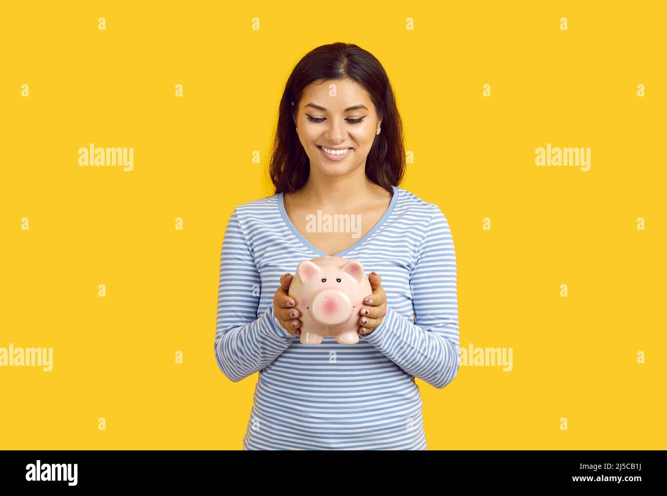 Joyful young casual woman holding piggy bank in form of pig isolated on yellow background. Stock Photo