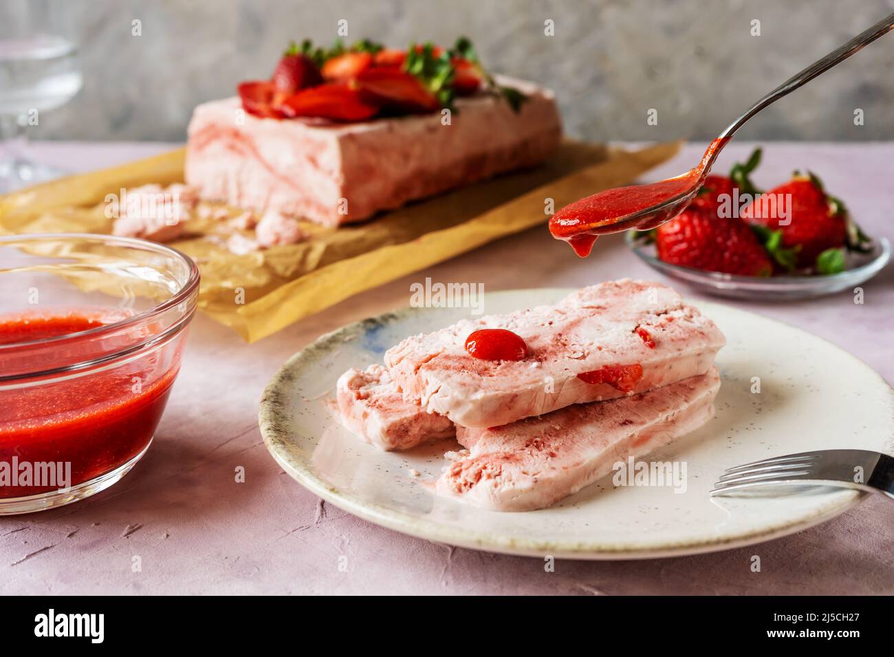 Italian strawberry dessert Semifreddo on plate with teaspoon pouring strawberry's sauce Stock Photo