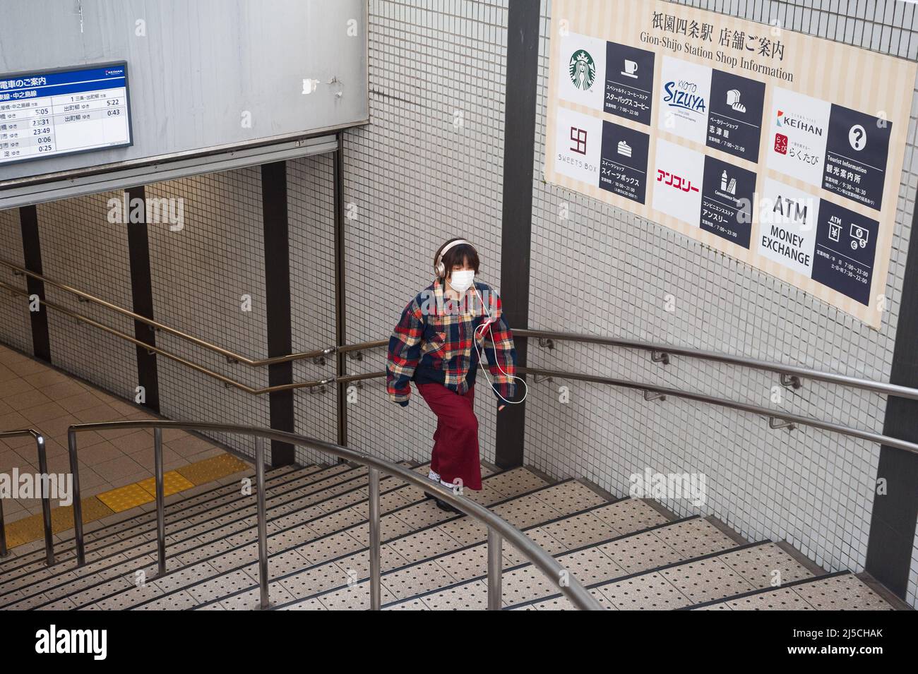 Dec. 23, 2017, Kyoto, Japan, Asia - A young woman wearing a mouth guard and headphones walks up a flight of stairs in a downtown subway station. [automated translation] Stock Photo