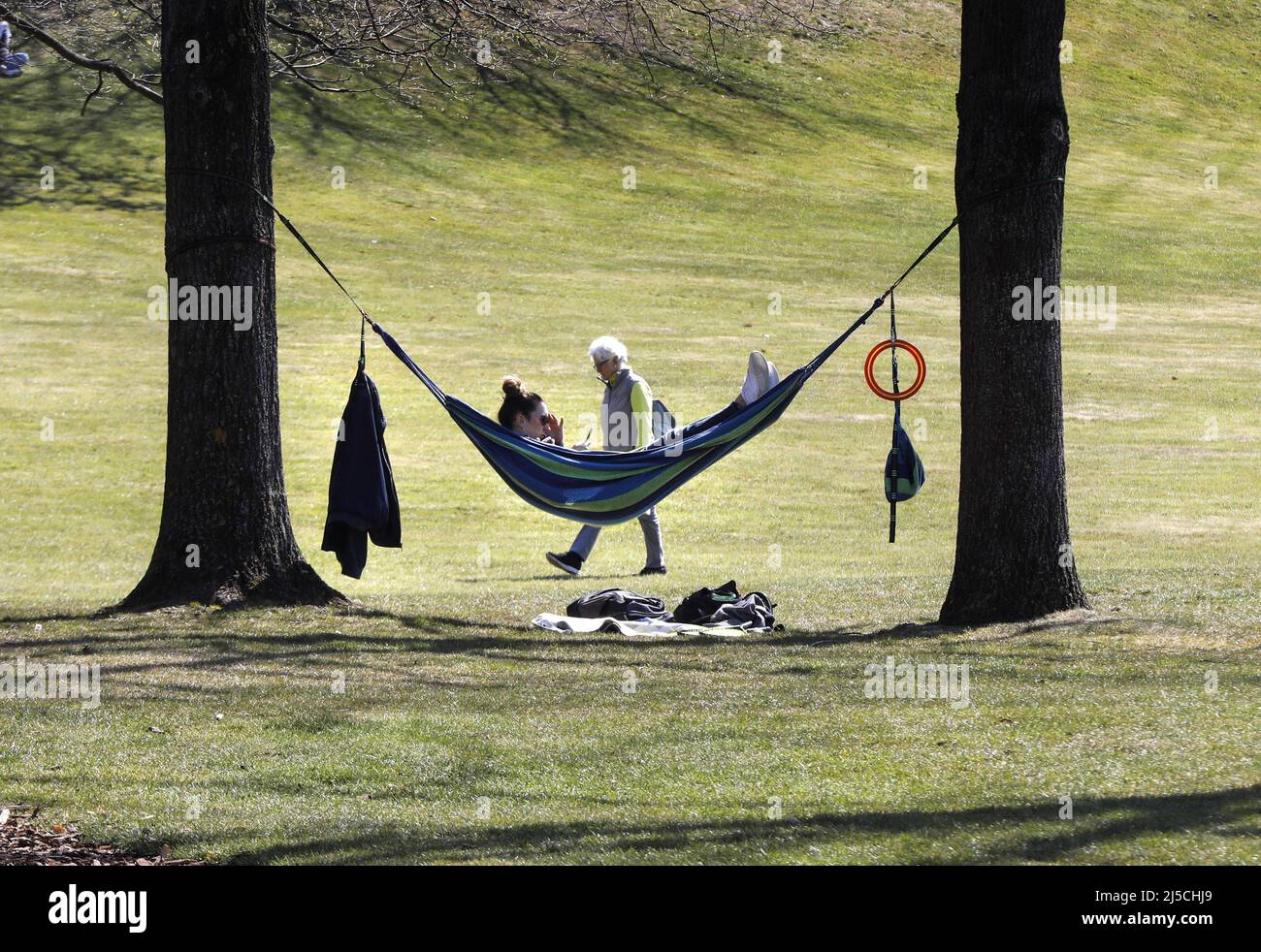 A woman lies in a hammock in a Berlin park and enjoys the spring-like weather. Police are checking parks to see if the Corona contact ban is being observed. In the meantime, the Berlin Senate had extended the contact ban in force due to the Corona pandemic by a few weeks. [automated translation] Stock Photo