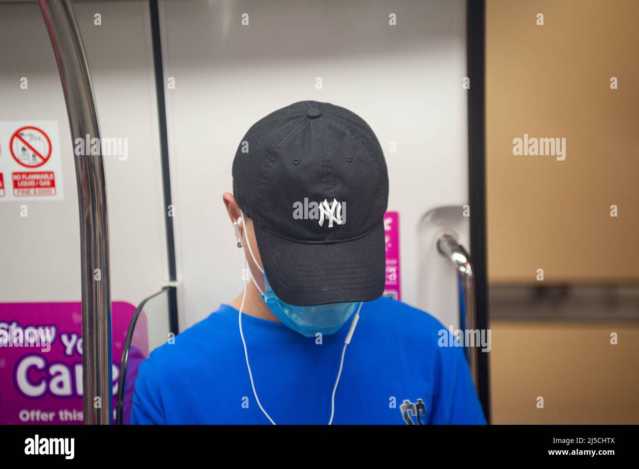 Feb. 28, 2020, Singapore, Republic of Singapore, Asia - A young man wears a respirator on a subway to protect himself from contracting the pandemic coronavirus. He is wearing a baseball cap with the logo of the New York Yankees. [automated translation] Stock Photo