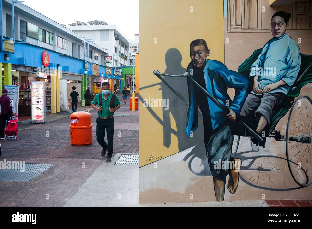 25.03.2020, Singapore, Republic of Singapore, Asia - A man walks past a mural of a traditional rickshaw in a pedestrian area in the Ang Mo Kio district. He is wearing a respirator mask to protect himself from contracting the pandemic coronavirus. [automated translation] Stock Photo