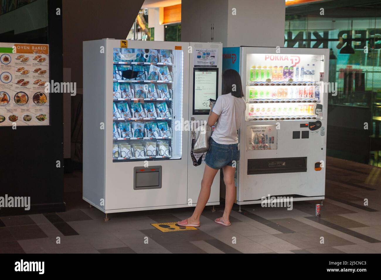 06/10/2020, Singapore, Republic of Singapore, Asia - A woman obtains a reusable mouthguard to prevent the spread of Covid-19 (coronavirus) from a government-issued vending machine at Kebun Baru community center where she scans her ID card. [automated translation] Stock Photo