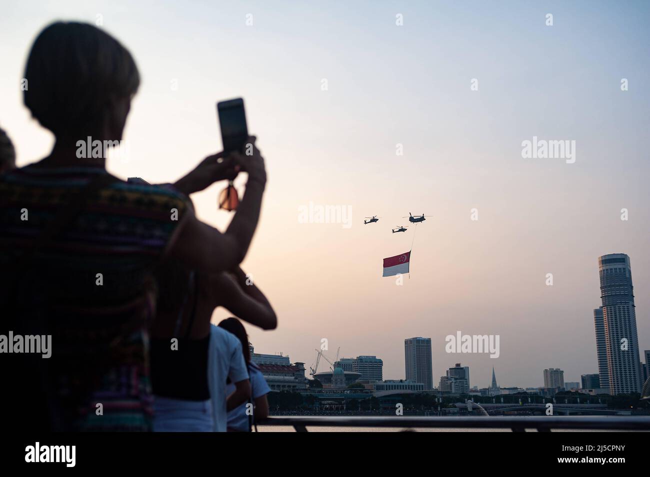 07/21/2018, Singapore, Republic of Singapore, Asia - Onlookers watch Air Force (RSAF) helicopters fly a giant state flag over skyscrapers in Marina Bay during a training flight in preparation for the upcoming National Day holiday on Aug. 9. [automated translation] Stock Photo