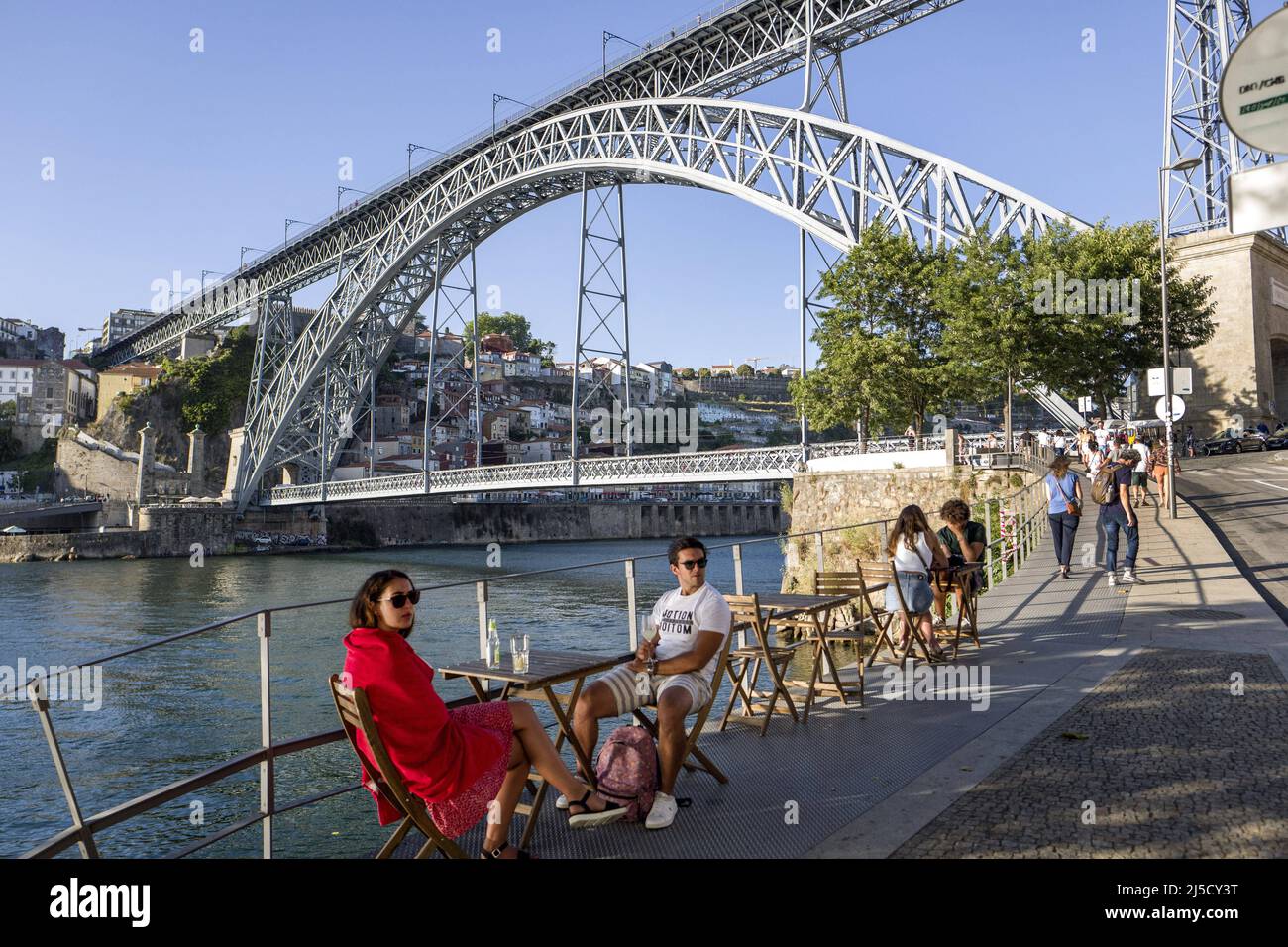 Portugal, Porto, 24.07.2020. Tourists on the river bank in Vila Nova de Gaia in Porto on 24.07.2020. The Luis I Bridge, also known as D. Luís I Bridge, is a truss arch bridge over the Douro River between Porto and Vila Nova de Gaia in Portugal. The construction of the bridge began in 1881 and was inaugurated on October 31, 1886 by King Louis I of Portugal (Dom Luís I), whose name it bears. [automated translation] Stock Photo