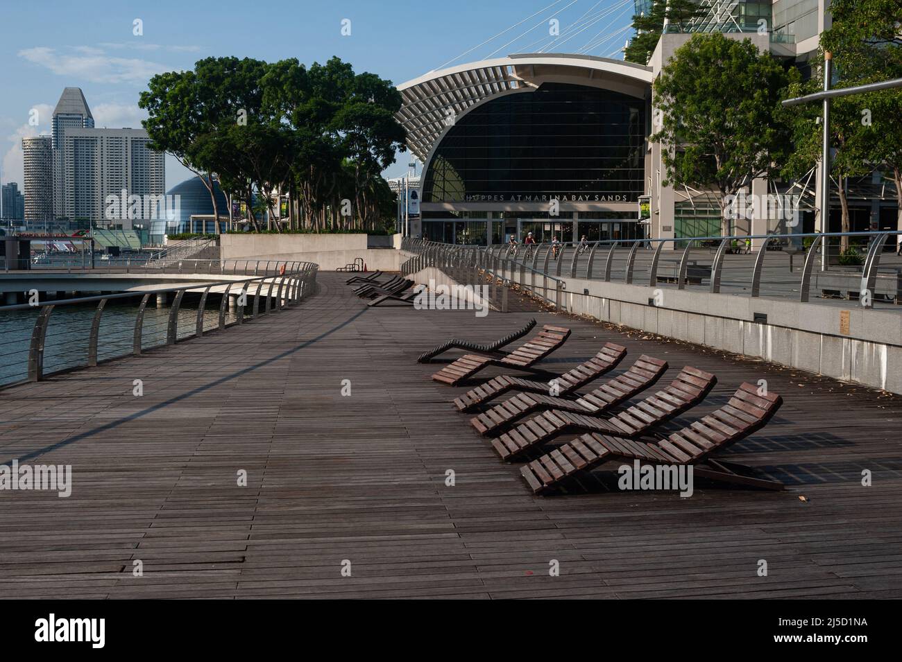 25.05.2021, Singapore, Republic of Singapore, Asia - Empty deck chairs along the waterfront in Marina Bay during the ongoing Corona crisis and The Shoppes shopping mall at Marina Bay Sands in the background, shortly after a new wave of infection has returned the Southeast Asian country to a lockdown-like state. This has resulted in further restrictions such as stricter border measures and entry requirements coupled with mandatory pre-testing and a negative test result on departure for all locals and permanent residents, as well as the closure of all elementary school, a ban on restaurant Stock Photo