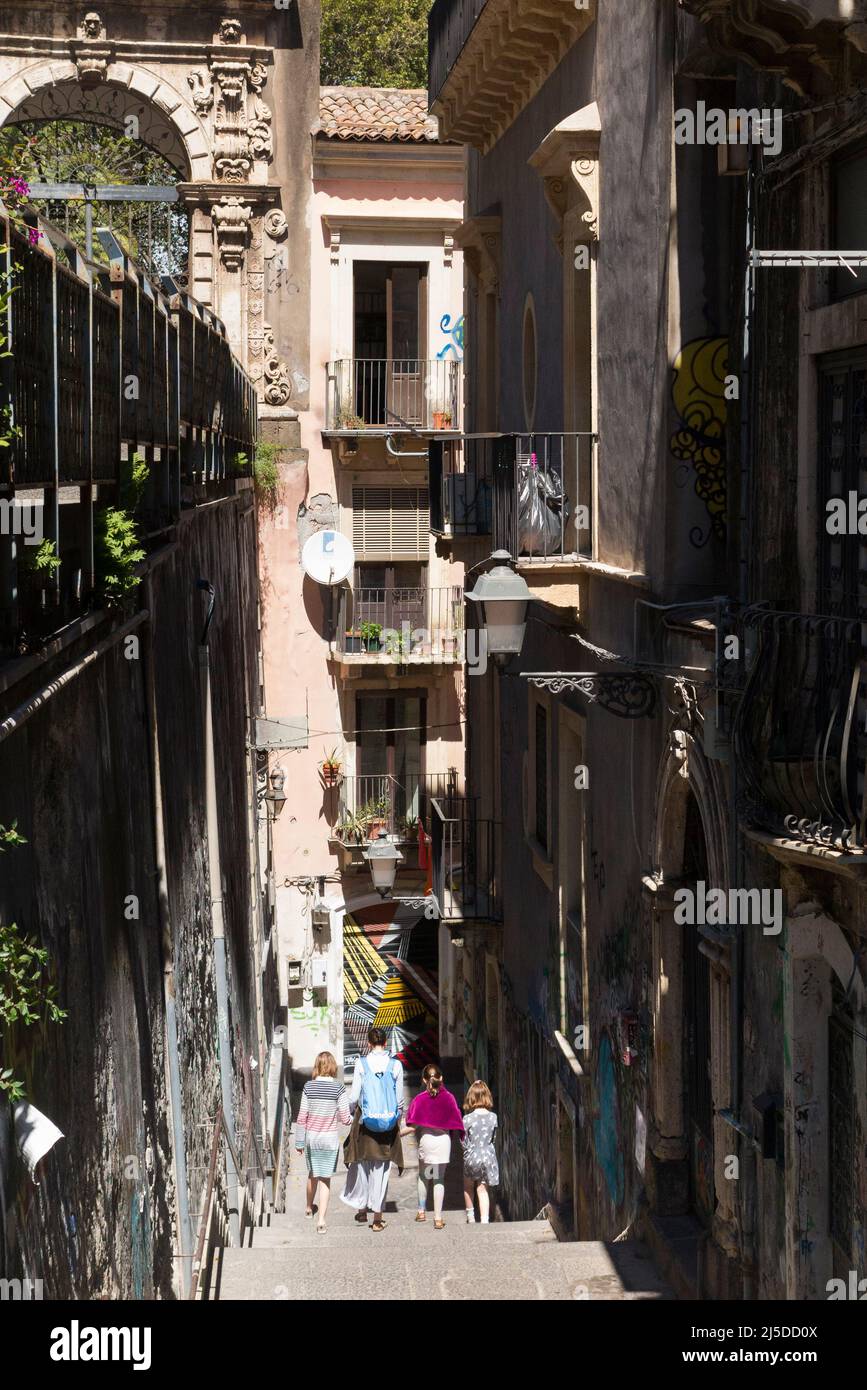 People including a tourist family descend sunken descending flight of steps on Via Penninello, City of Catania, Sicily. Italy. Seen from Via Crociferi. (129) Stock Photo