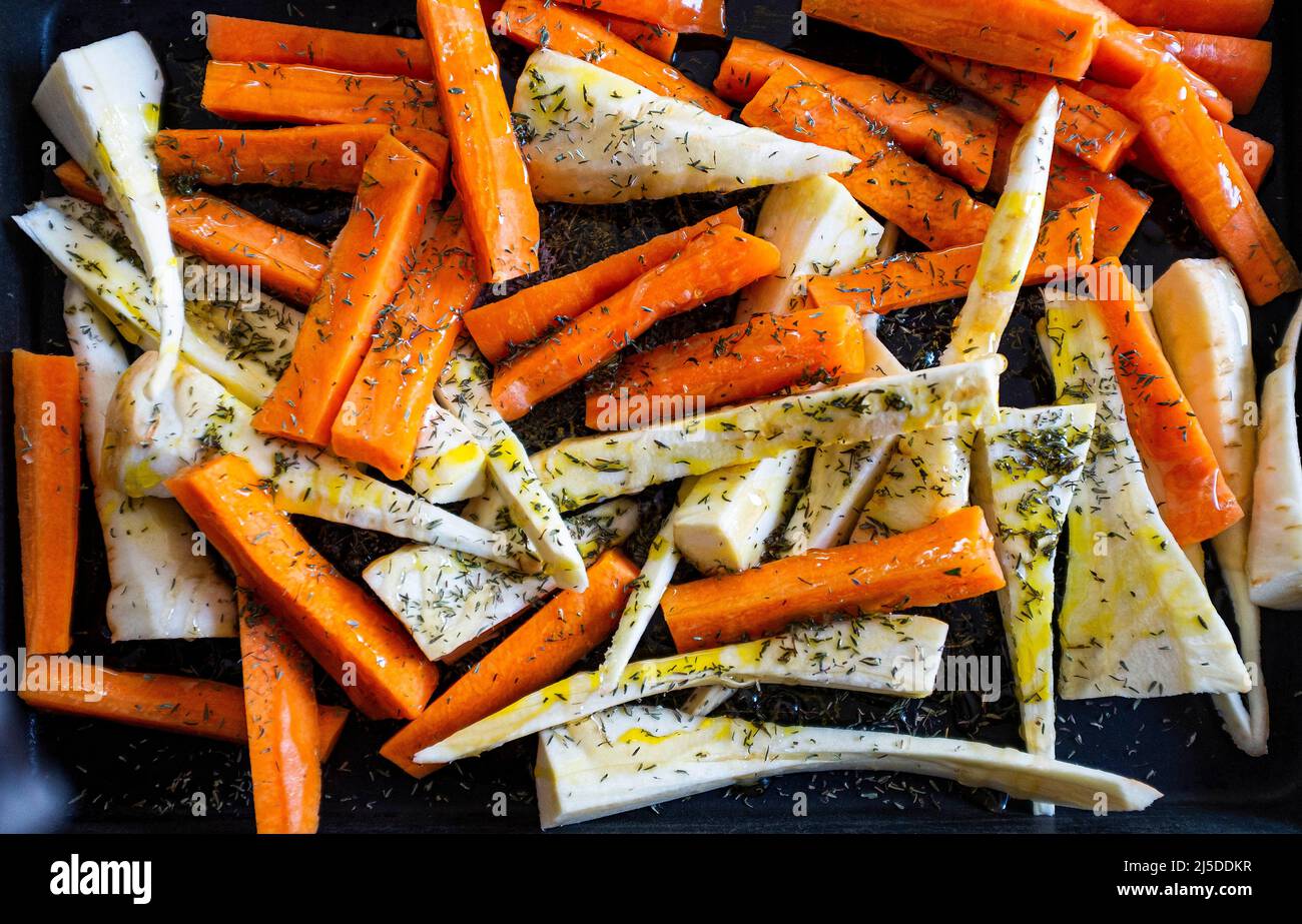 Carrots and parsnips cut into strips with honey olive oil and thyme prepared for roasting Stock Photo