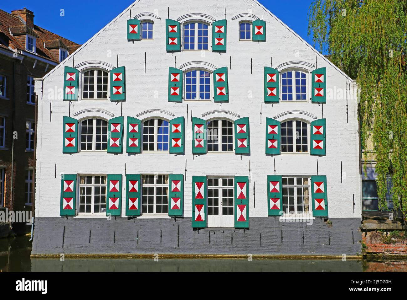 Closeup of ancient waterfront house facade, many glass windows, open exterior board batten shutters painted in triangle red white design - Lier, Belgi Stock Photo